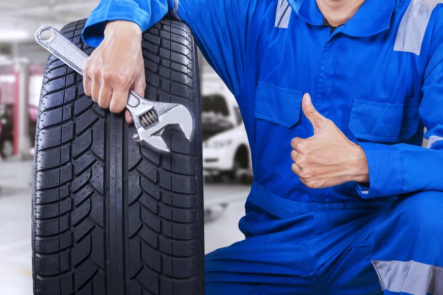 Car Servicing - stock-photo-technician-with-a-blue-workwear-holding-a-wrench-and-a-tire-while-showing-thumb-up-262878917-min